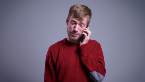 Retrato de close-up de homem caucasiano atraente falando no telefone e sorrindo na frente da câmera — Vídeo de Stock