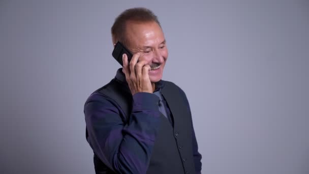 Крупный план портрета счастливого старшего кавказца разговаривающего по телефону на фоне изолированного на сером фоне — стоковое видео