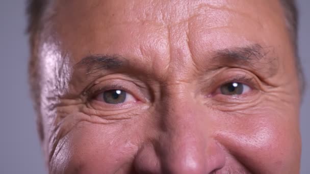 Primer plano de los ojos grises masculinos caucásicos arrugados senior mirando directamente a la cámara con expresión facial feliz — Vídeo de stock