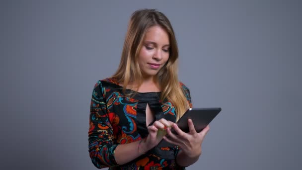 Vértes portré fiatal pozitív kaukázusi nő segítségével a tabletta, és bemutatja a zöld képernyőn a kamera mosolyogva — Stock videók