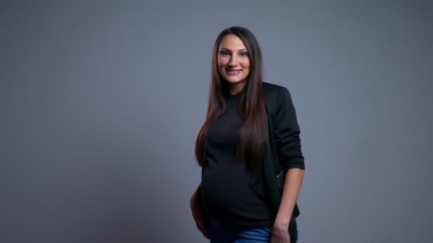 Nahaufnahme Porträt einer jungen glücklichen schwangeren kaukasischen Frau, die lächelnd ihren Bauch hält und in die Kamera schaut — Stockvideo