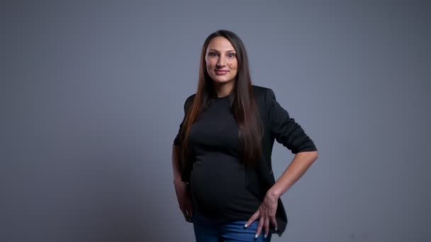 Nahaufnahme Porträt einer schwangeren jungen kaukasischen Frau, die aufgeregt in die Kamera blickt und ihre Hände auf den Hüften trägt — Stockvideo