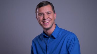 Portre portre Genç beyaz adam neşeyle gülümseyen ve kameraya bakarken gülüyor.