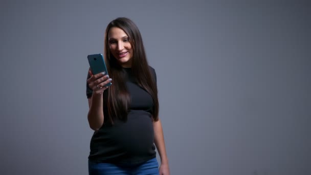 Closeup portret van de jonge Kaukasische zwangeren met een video-oproep op de telefoon glimlachend en tonen haar buik — Stockvideo