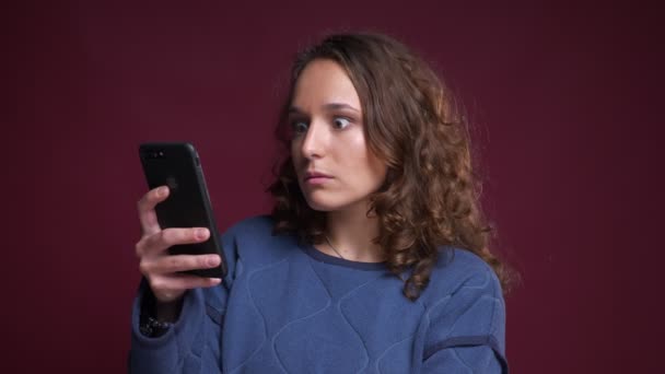 Крупный план портрета молодой кавказской женщины, использующей телефон и внезапно расстраивающейся и разочарованной — стоковое видео