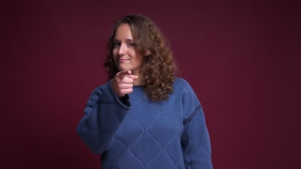 Detailní portrét youngpositive Kavkazský žena usmívající se dívá rovně a polohovací bodů prstem na kameru — Stock video
