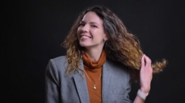 Çekici genç kadın gülümseyen flört ve doğruca kameraya bakarak kahverengi kıvırcık saçları ile oynamak portre portre
