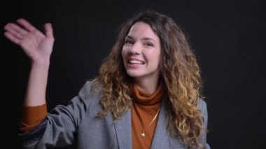 Closeup portrait of friendly happy young female looking at camera smiling and waving her hand saying hello