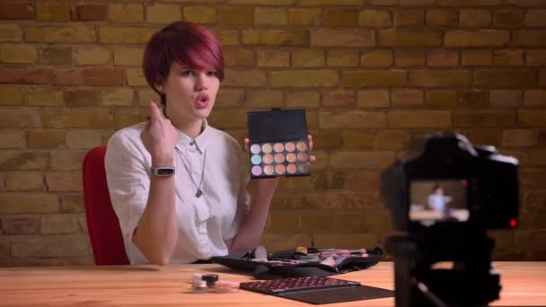 Portræt af ung korthåret kvindelig skønhedsblogger smukt taler om hendes værktøjer i kameraet på bricken væg baggrund . – Stock-video