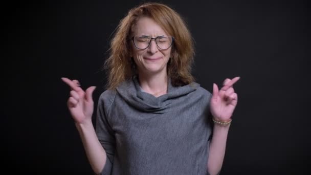 Retrato de primer plano de la esperanzada mujer caucásica de mediana edad con los dedos cruzados y rezando — Vídeo de stock