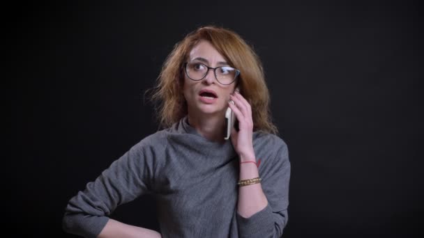 Portret zbliżenie dorosły kaukaski kobieta o rozmowy na telefon uśmiechający się i śmiejąc się z tłem, na czarnym tle — Wideo stockowe
