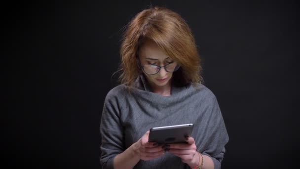 Closeup portret van middelbare leeftijd moderne vrouwelijke te typen op de tablet terloops met geïsoleerd op zwarte achtergrond — Stockvideo