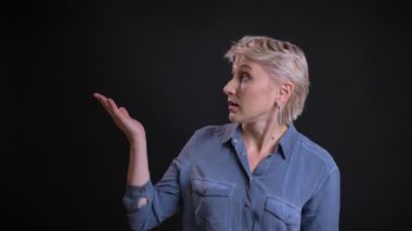 Orta yaşlı beyaz kadın belirsiz bir yüz ifadesi ile bir proje sunan sağ eliyle işaret Closeup portresi.