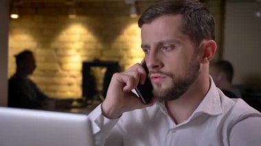 Telefonda laptop önünde oturan bir tartışma sahip genç konsantre beyaz iş adamı closeup