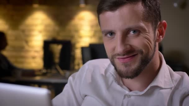 Closeup of young cheerful caucasian businessman typing on the laptop looking at camera and smiling. — Stock Video