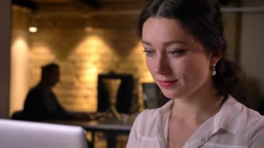 Genç çekici başarılı kadın ofis çalışanının işyerinde dizüstü bilgisayara yazarak yakın çekim portresi.