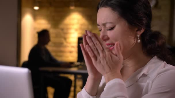 Close-up van jonge ziek Kaukasische vrouwelijke beambte niezen terwijl u op de laptop binnenshuis op de werkplek — Stockvideo