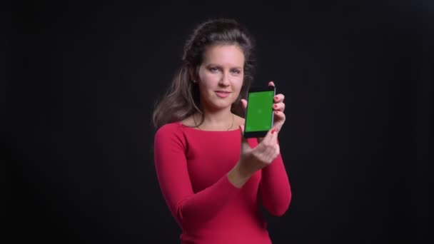 Портрет білої жінки в червоному посміхаючись показує зелений екран планшета в камеру на чорному тлі . — стокове відео