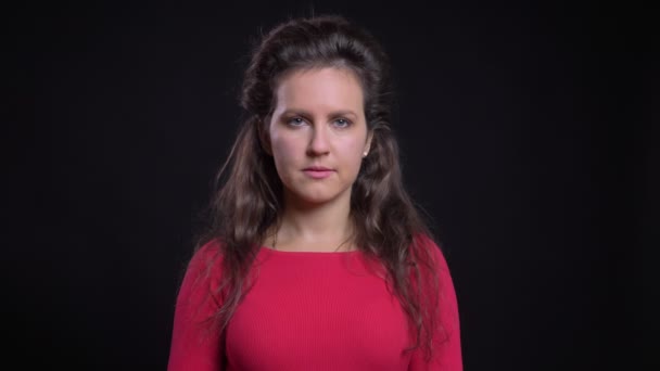 Portrait de femme caucasienne en rouge regardant calmement dans la caméra sur fond noir . — Video