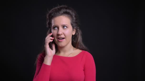 Retrato de mujer caucásica en rojo alegremente hablando usando teléfono inteligente sobre fondo negro . — Vídeos de Stock