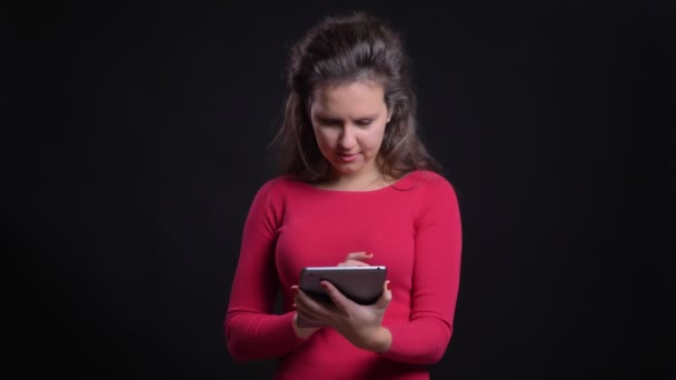 Retrato de mujer caucásica en rojo mirando sonriente en la tableta sobre fondo negro . — Vídeo de stock