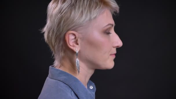 Profilé rapproché portrait de caucasienne blonde femelle tournant et regardant droit devant la caméra avec fond isolé sur noir — Video