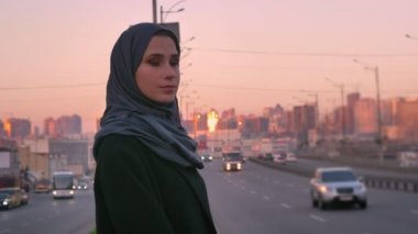 Yolun kenarında kalan ve kameraya ile akşam kentsel şehir arkasında seyir hijab genç çekici Müslüman closeup portresi
