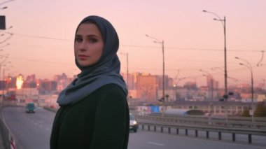 Kameraya bakarak ve geçen arabaların arkasında kentsel city ile tarafından ayakta poz hijab genç çekici Müslüman closeup portresi