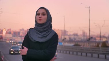 Kollarını doğruca kameraya bakarak ve geçen arabaların tarafından ayakta göğsünde ile genç çekici Müslüman erkek portre portre