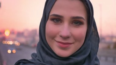 Gülümseyen ve kameraya kentsel şehir ile arka plan üzerinde seyir hijab genç çekici Müslüman kadın portresi portre