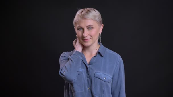 Primo piano ritratto di affascinante donna caucasica con i capelli corti biondi sorridente e strofinando il collo guardando la fotocamera — Video Stock