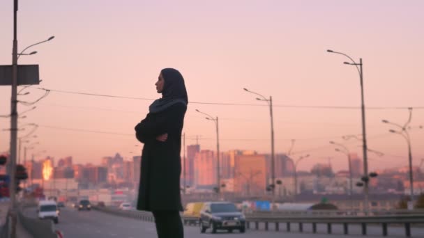 Widok z tyłu portret młodego muzułmanina atrakcyjne w hidżab stoi przy drodze i zwracając się do aparatu z miejskich miasta z tyłu — Wideo stockowe