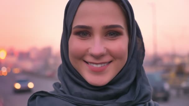 Portret zbliżenie młodych atrakcyjnych kobiet muzułmańskich w hidżab uśmiecha się wesoło i patrząc prosto w obiektyw kamery z miejskiego miasta z tyłu — Wideo stockowe