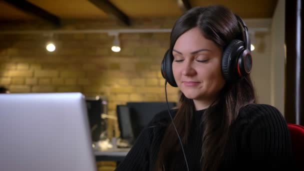 Vértes portréja felnőtt kaukázusi pozitív üzletasszony fejhallgató gépelés a számítógépen, és zenét hallgatni — Stock videók
