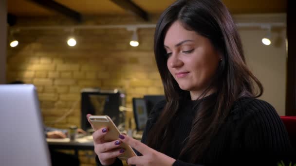 Primer plano retrato de adulto alegre mujer de negocios caucásica navegando por teléfono en frente de la computadora portátil y sonriendo — Vídeos de Stock