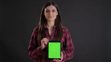 Genç beyaz uzun saçlı kız gülümseyerek dik tablet yeşil ekran siyah arka plan üzerinde gösterilen portresi.