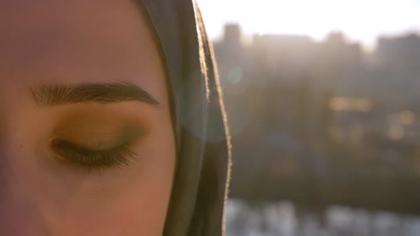 Крупним планом портрет молодої жінки в Хіджабі дивиться прямо на камеру з містом на спині. Відкриття і закриття очей — стокове відео