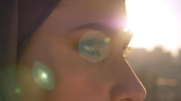 Closeup portrait of young beautiful female eyes looking forward. Woman in hijab with sun shining on the background — Stock Video
