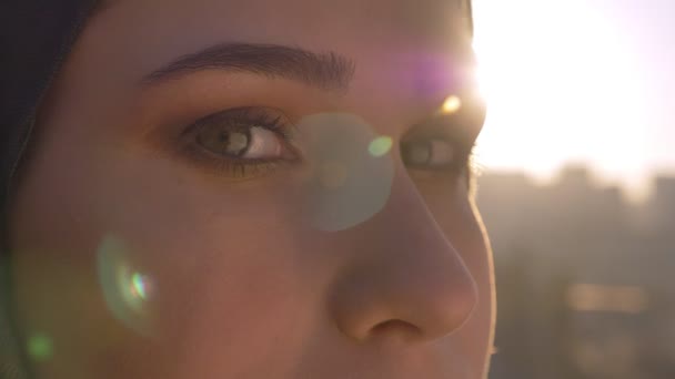 Retrato de close-up de jovem fêmea em hijjab olhando para a frente e para a câmera com o sol brilhando no fundo — Vídeo de Stock