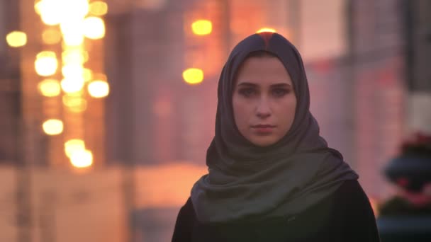 Vértes portré fiatal vonzó női hidzsáb nézett egyenesen a kamera, a szép csillogó városi város, a háttérben — Stock videók