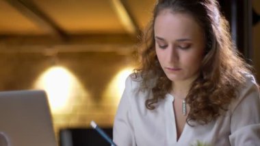 Yakın çekim dikkatle laptop ile çalışmaya ve notlar not defterinde office içine yapım genç kıvırcık saçlı kadın portresi.