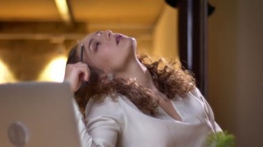 Yakın çekim portre genç kıvırcık saçlı kadın son derece koltuğa uzanmış ve onun yorgunluk gösterilen ofiste bored.