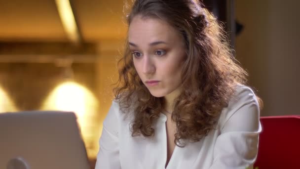 Närbild porträtt av unga curly-haired kvinna eftertänksamt arbetar med laptop i office. — Stockvideo