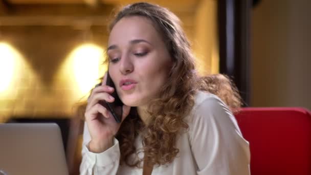 Close-up retrato de mulher de cabelos encaracolados emocionais alegremente falando no celular no escritório . — Vídeo de Stock