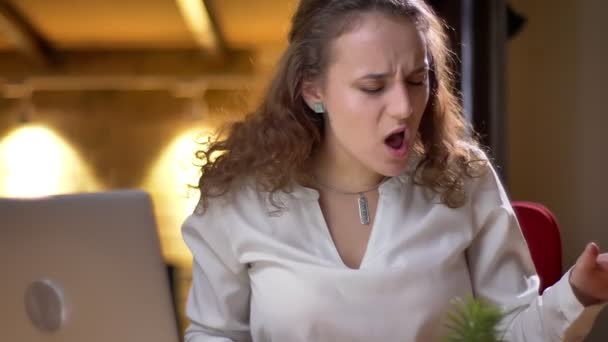 Portrait of young curly-haired woman joyfully dancing and singing in her seat in office. — Stock Video