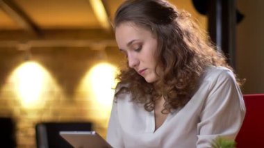 Dikkatle tablet izliyor ve kamera ofiste onun gözlerine yükselterek genç kıvırcık saçlı işkadını portresi.