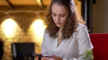 Genç kıvırcık saçlı işkadını dikkatle kredi kartı ve smartphone kullanarak işlemleri gerçekleştirme portresi.
