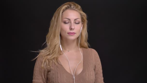 Retrato de mulher caucasiana de cabelos compridos alegre em fones de ouvido dançando lentamente à música em fundo preto . — Vídeo de Stock