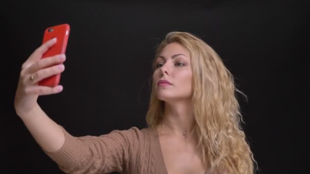 Portret van prachtige Kaukasische langharige vrouw maken selfie-foto's op smartphone op zwarte achtergrond. — Stockvideo