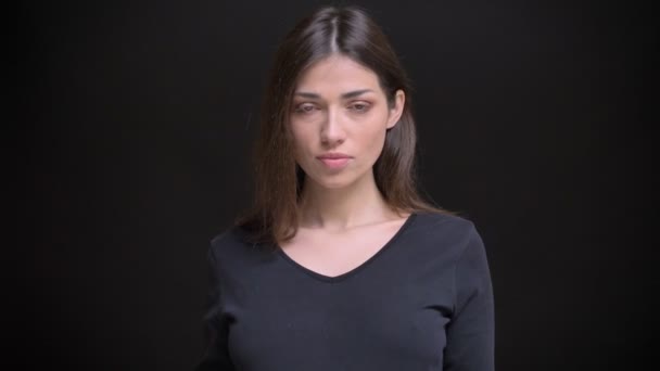 Porträt eines jungen kaukasischen langhaarigen brünetten Mädchens, das ernsthaft in die Kamera auf schwarzem Hintergrund schaut. — Stockvideo